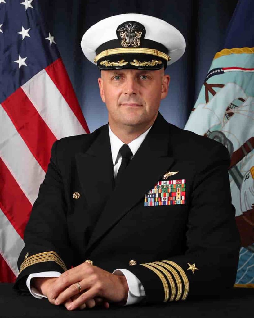 a portrait of Captain JJ "Yank" Cummings. He is seated in front of an American flag and the flag of the US Navy.