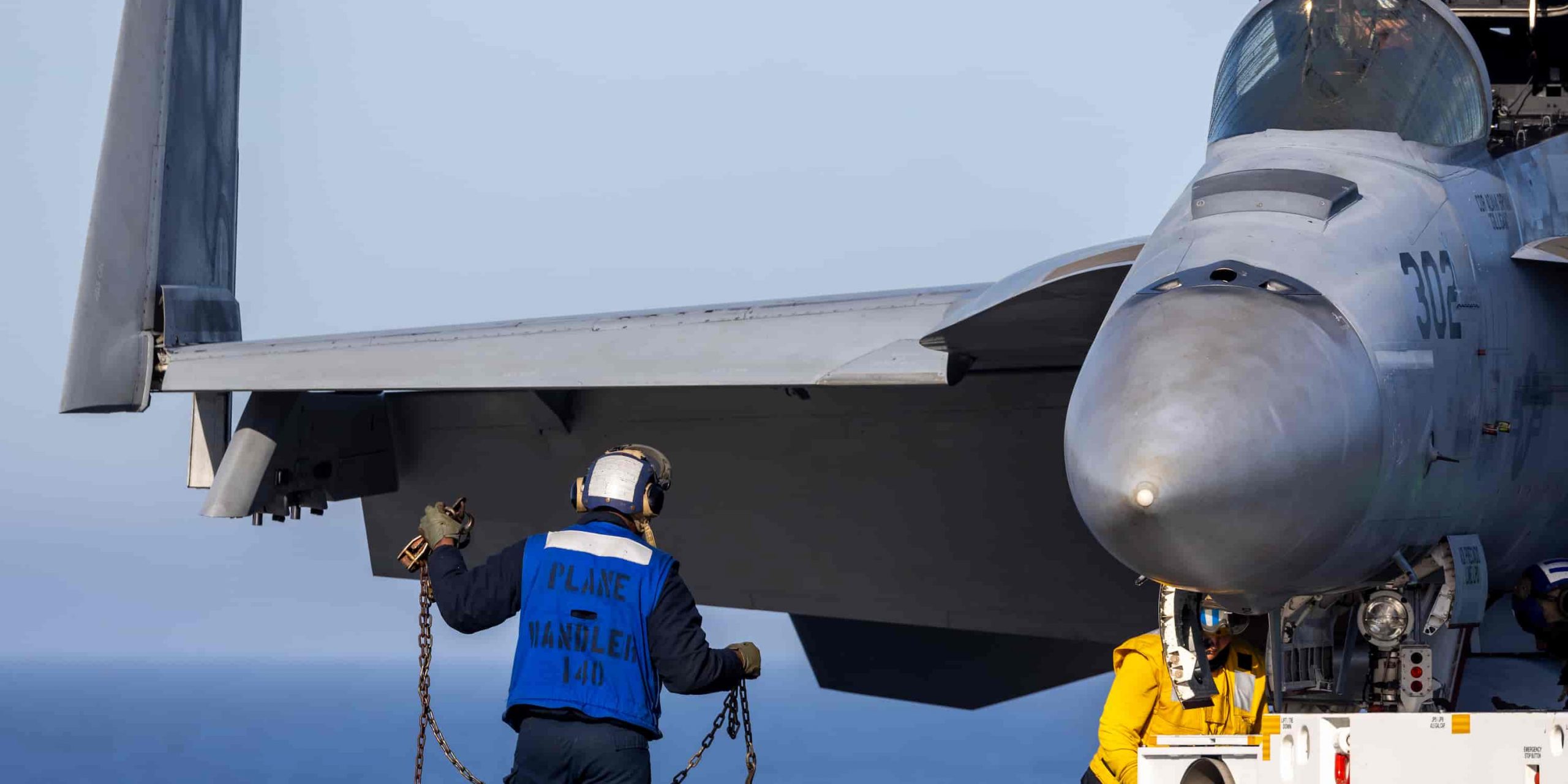 a "blue" flight deck officer stands in front of a jet's wing