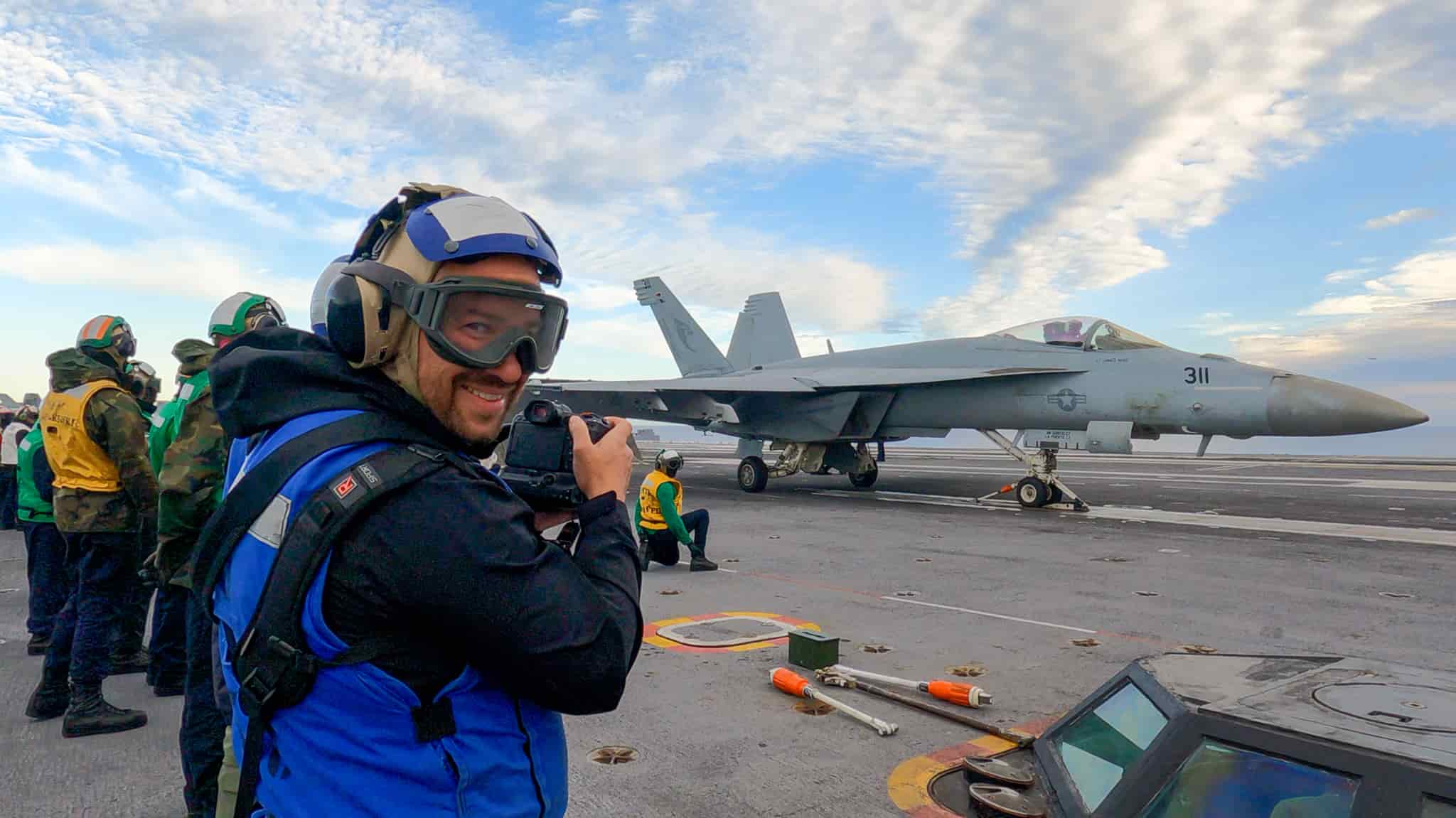 photographer kenton vanduyne stands in a blue flight deck crew vest holding a camera