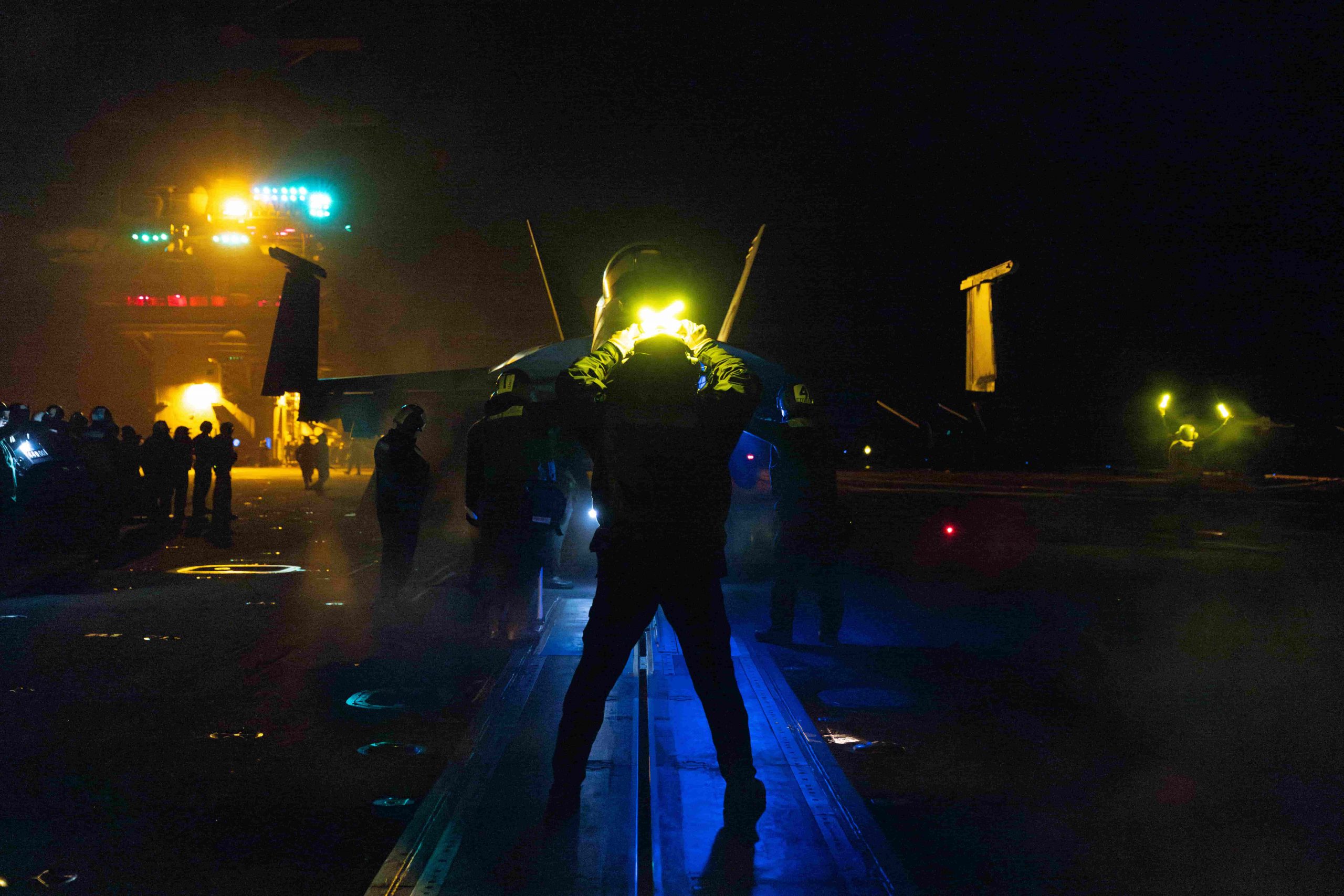 a flight deck officer stands in front of a jet with light wands in his hands. lights glow through the smoke and fog, creating and eerie, exciting atmosphere.