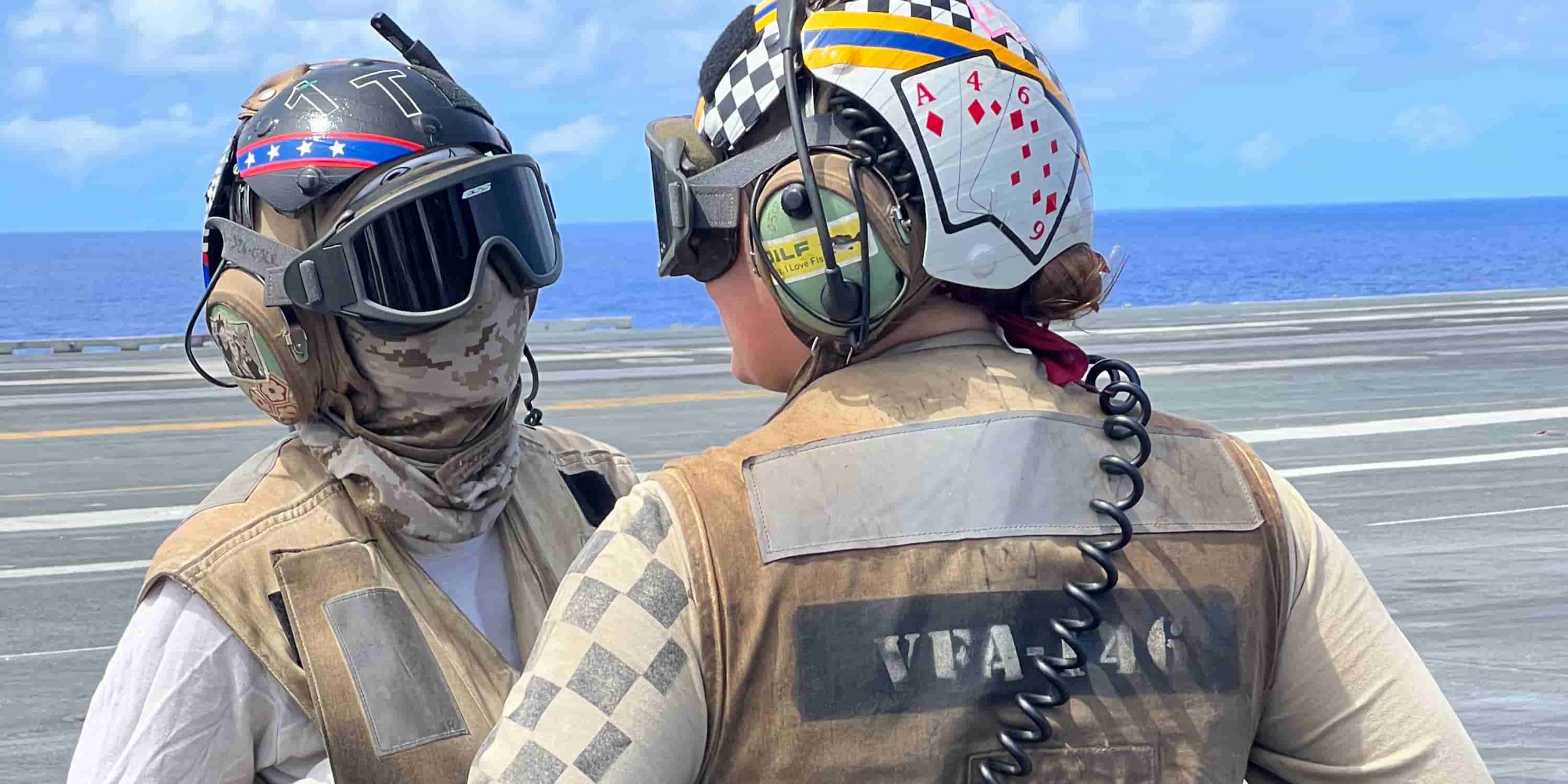 two flight deck crew members in white stand discussing the task at hand.